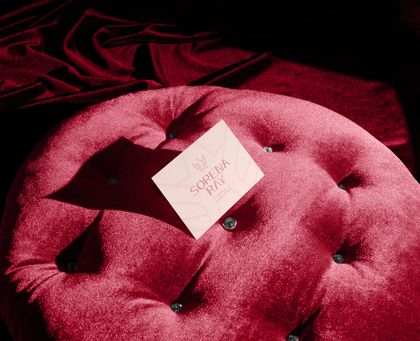 Cartão de visitas rosa da Sorena Ray sobre um puff de veludo vermelho